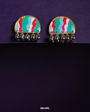 the Aabshaar stud earrings featuring a vibrant, hand-painted semi-circle design in teal, red, white, and green, edged with gold and adorned with dangling oxidized silver ghungroos, set against a deep purple background — Muselot.