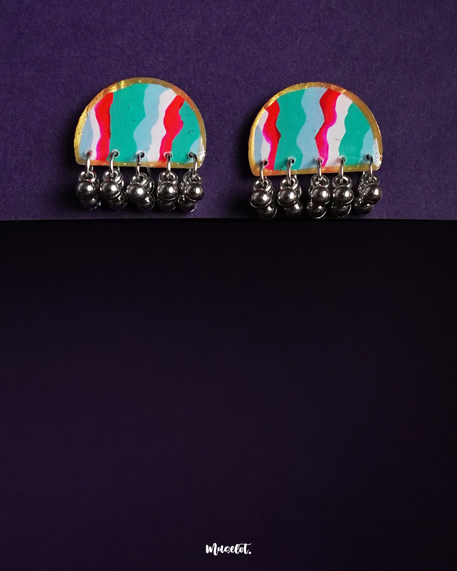 the Aabshaar stud earrings featuring a vibrant, hand-painted semi-circle design in teal, red, white, and green, edged with gold and adorned with dangling oxidized silver ghungroos, set against a deep purple background — Muselot.