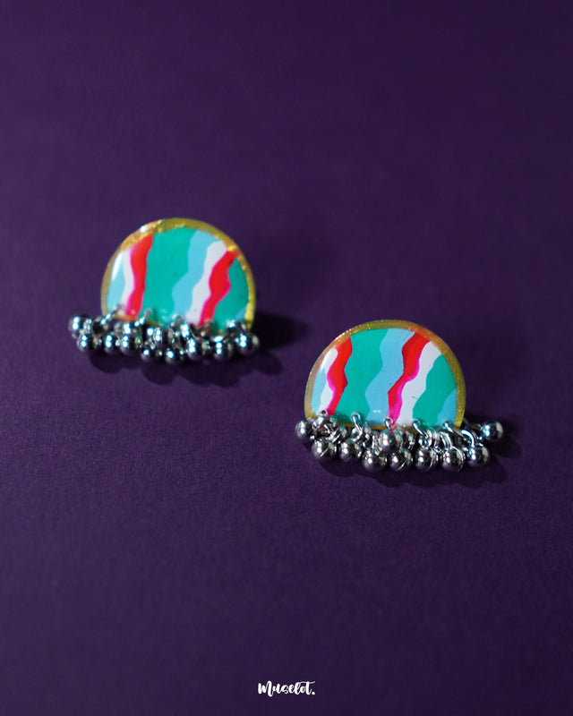Aabshaar stud earrings placed flat with a focus on their vibrant hand-painted details — rich teal, bold red, and soft white. The antique silver base and dainty ghungroo drops evoke a handcrafted heritage appeal — Muselot.