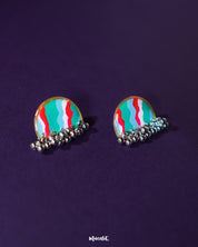 Aabshaar stud earrings displayed against a neutral backdrop, highlighting their floral pattern in vivid hues of teal, red, and white. The antique-finished base and tiny ghungroos below add a traditional charm to this intricate handmade pair — Muselot.
