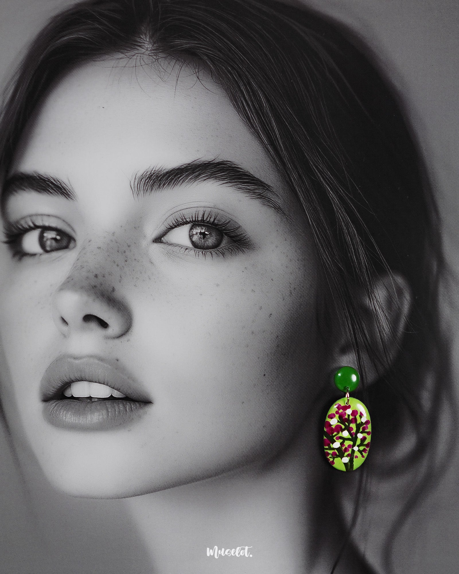 A woman wears the Baaghani handmade drop earrings, highlighting the lively floral design with white and magenta buds on a green base, showcasing the craftsmanship and charm of these statement accessories — Muselot.