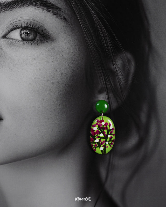 Closeup of a woman wearing the Baaghani handmade drop earrings, highlighting the vivid green base adorned with delicate white and magenta floral motifs, showcasing their vibrant charm and intricate hand-painted details — Muselot.