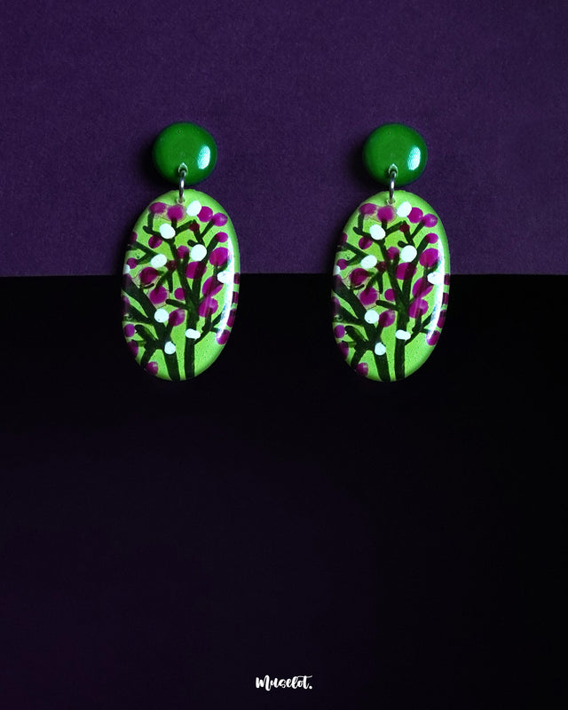 Baaghani drop earrings featuring an intricate floral pattern of white and magenta buds on a rich green oval base, paired with matching green studs and set against a dramatic purple-black backdrop — Muselot.