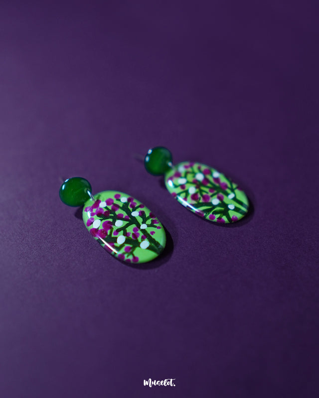 A pair of Baaghani green floral drop earrings resting against a neutral backdrop, showcasing their petal-inspired design in deep green with pink and white floral detailing, highlighting the handcrafted charm and nature-inspired elegance — Muselot.