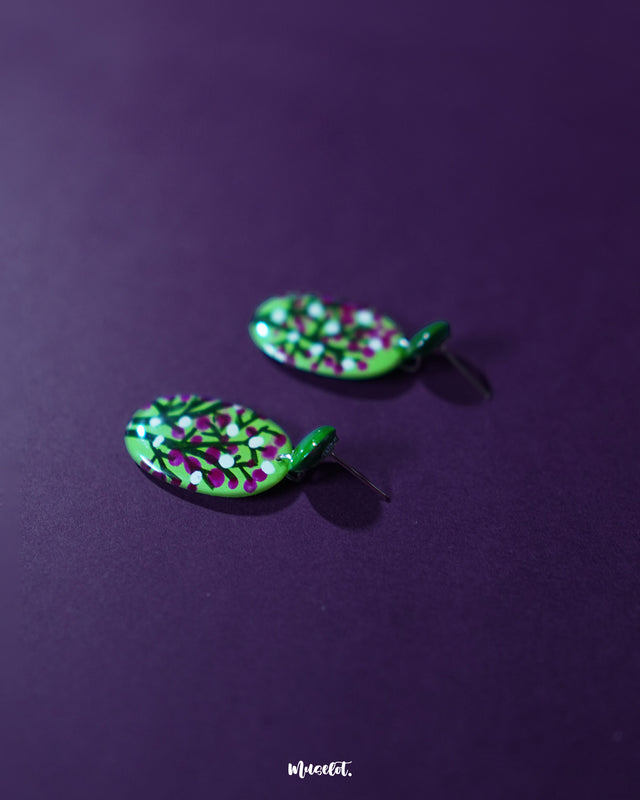 Baaghani green floral drop earrings laid flat on a textured surface, highlighting the delicate floral accents and the handcrafted green base that brings out an earthy, graceful charm — Muselot.