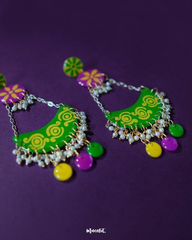 A close-up shot of Baharaan green chandbali earrings placed on a soft surface, highlighting the intricate curves, dangling beads, and glossy hand-painted finish that showcases traditional elegance — Muselot.