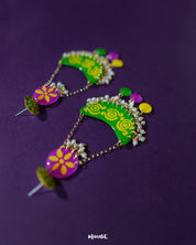 A pair of Baharaan green chandbali earrings placed on a purple fabric backdrop, highlighting their crescent shape, delicate golden detailing, and dangling accents, showcasing a handcrafted charm rooted in traditional design — Muselot.