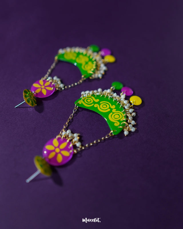 A pair of Baharaan green chandbali earrings placed on a purple fabric backdrop, highlighting their crescent shape, delicate golden detailing, and dangling accents, showcasing a handcrafted charm rooted in traditional design — Muselot.