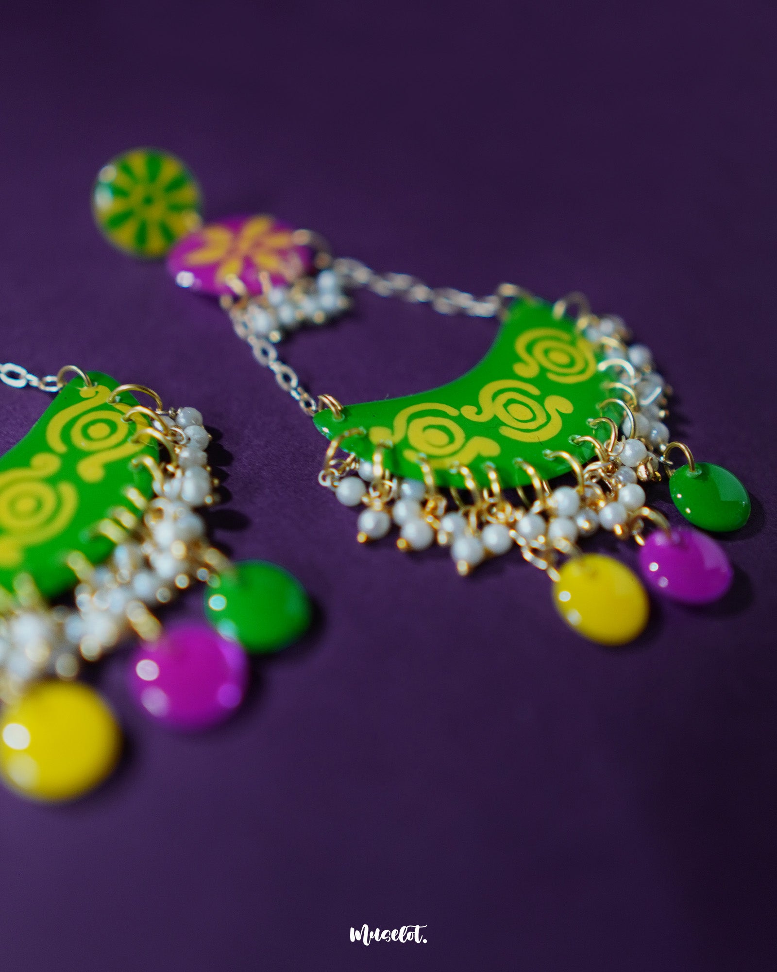A close-up of the Baharaan green chandbali earrings resting on a soft purple surface, showcasing the intricate hand-painted details, crescent silhouette, and metallic golden accents that highlight their festive elegance — Muselot.
