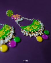 A close-up of the Baharaan green chandbali earrings resting on a soft purple surface, showcasing the intricate hand-painted details, crescent silhouette, and metallic golden accents that highlight their festive elegance — Muselot.