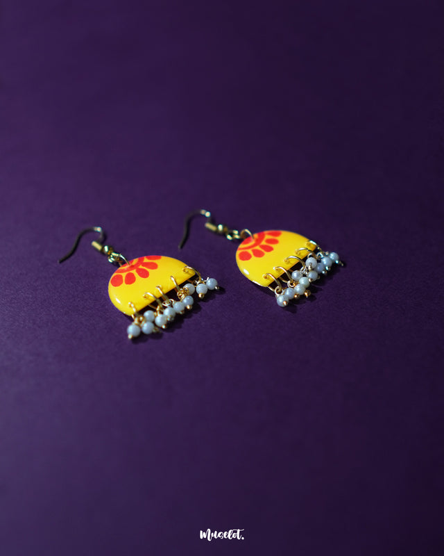 A pair of Basantika yellow floral hook earrings displayed on a rich purple backdrop, showcasing their vibrant red and yellow floral design with tiny bead detailing that adds a festive, handcrafted charm — Muselot.
