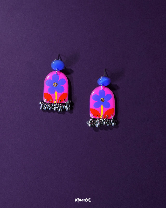 Benazir floral earrings beautifully arranged against a rich purple background, showcasing delicate purple flowers and vibrant red leaves that create a striking contrast, enhancing their artistic elegance — Muselot