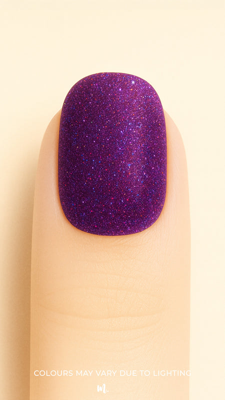 A close-up shot of a model’s finger wearing Berry Cosmos Glitter nail stickies, showcasing a deep purple base filled with fine multicolor glitter specks in pink, blue, and violet. The design highlights the cosmic sparkle and glossy galaxy-like finish that makes this glitter nail art stand out – Muselot.