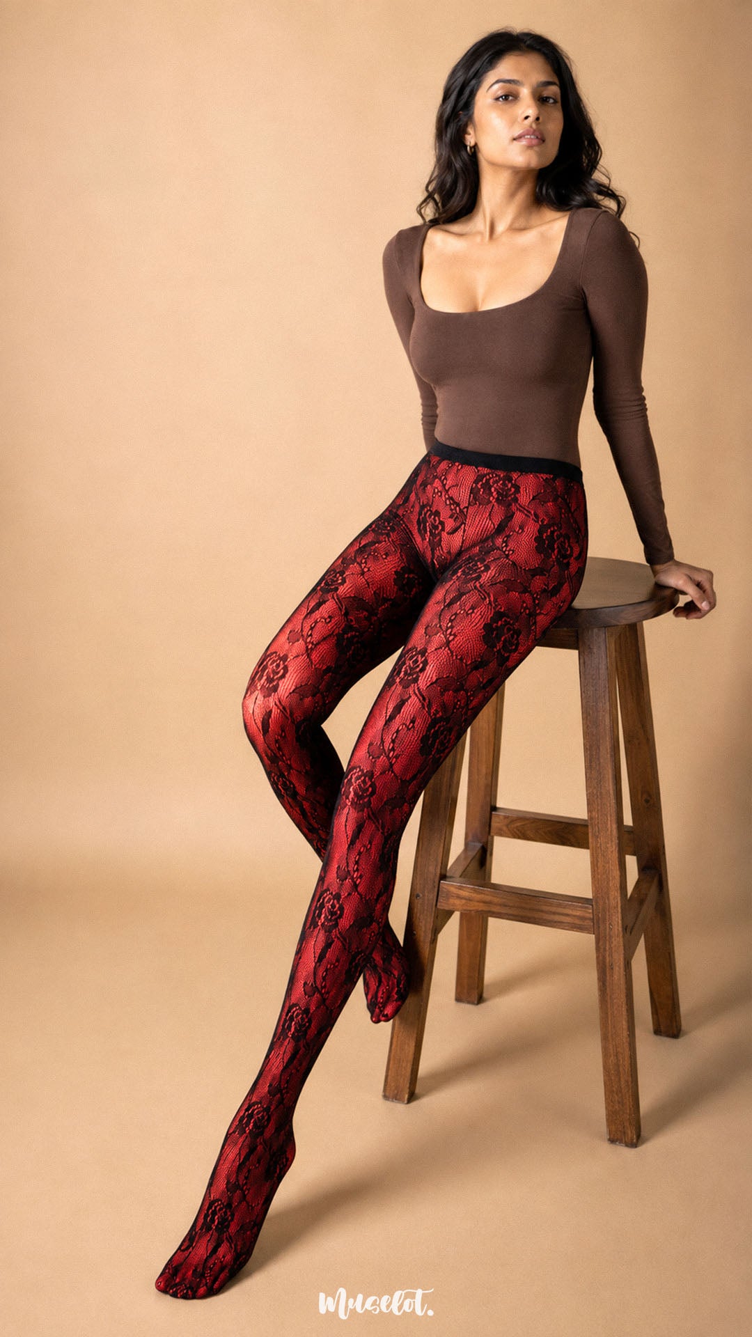 The model layers black rose designer lace stockings over red opaque stockings while seated, showcasing the bold red-and-black floral contrast of the Sinful Rose combination – Muselot.
