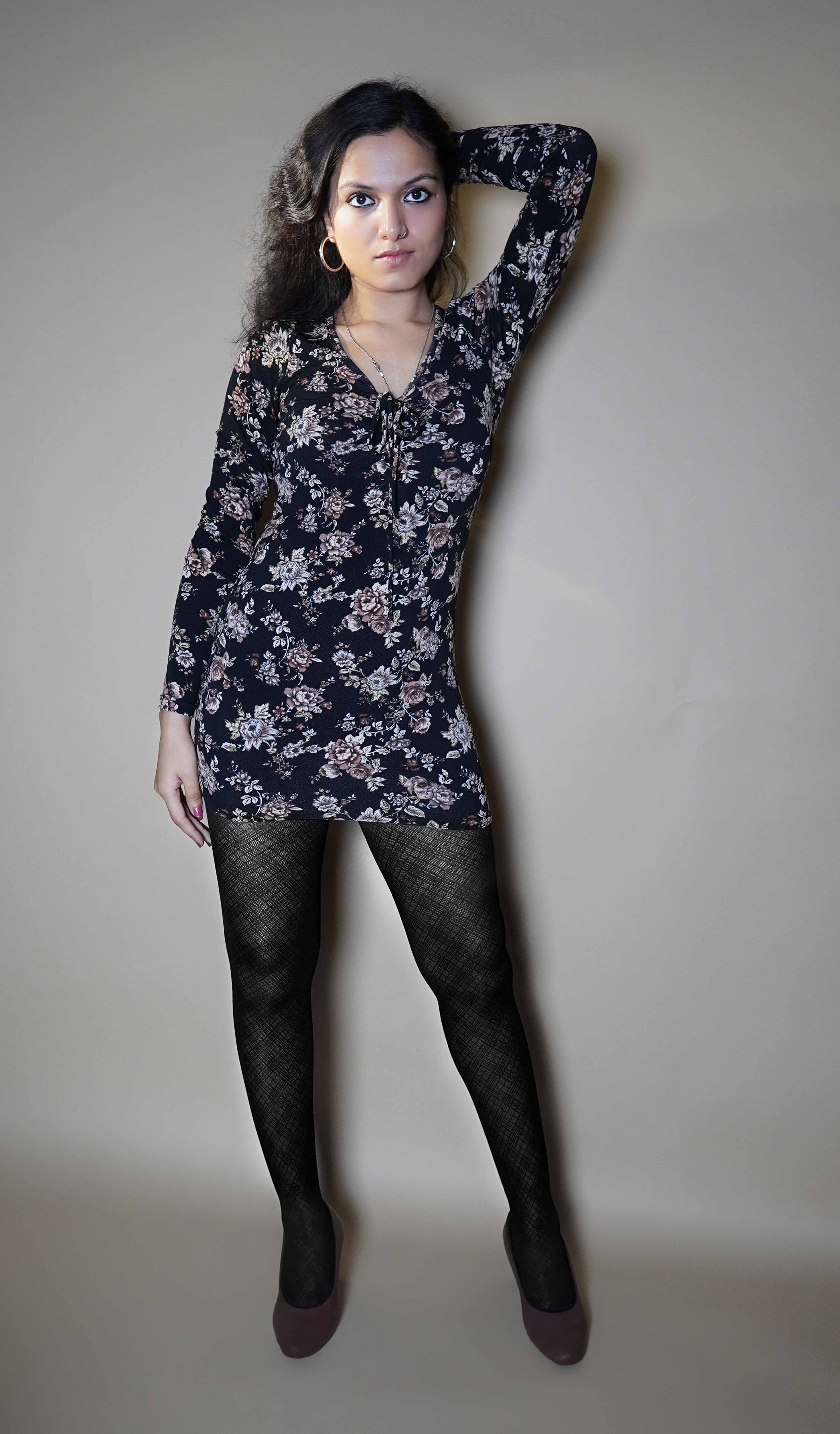 A woman wearing patterned sheer stocking in black color, posing with her hand up and at the back of her head as the other hangs at her side, highlighting the stretchable breathable material-Muselot