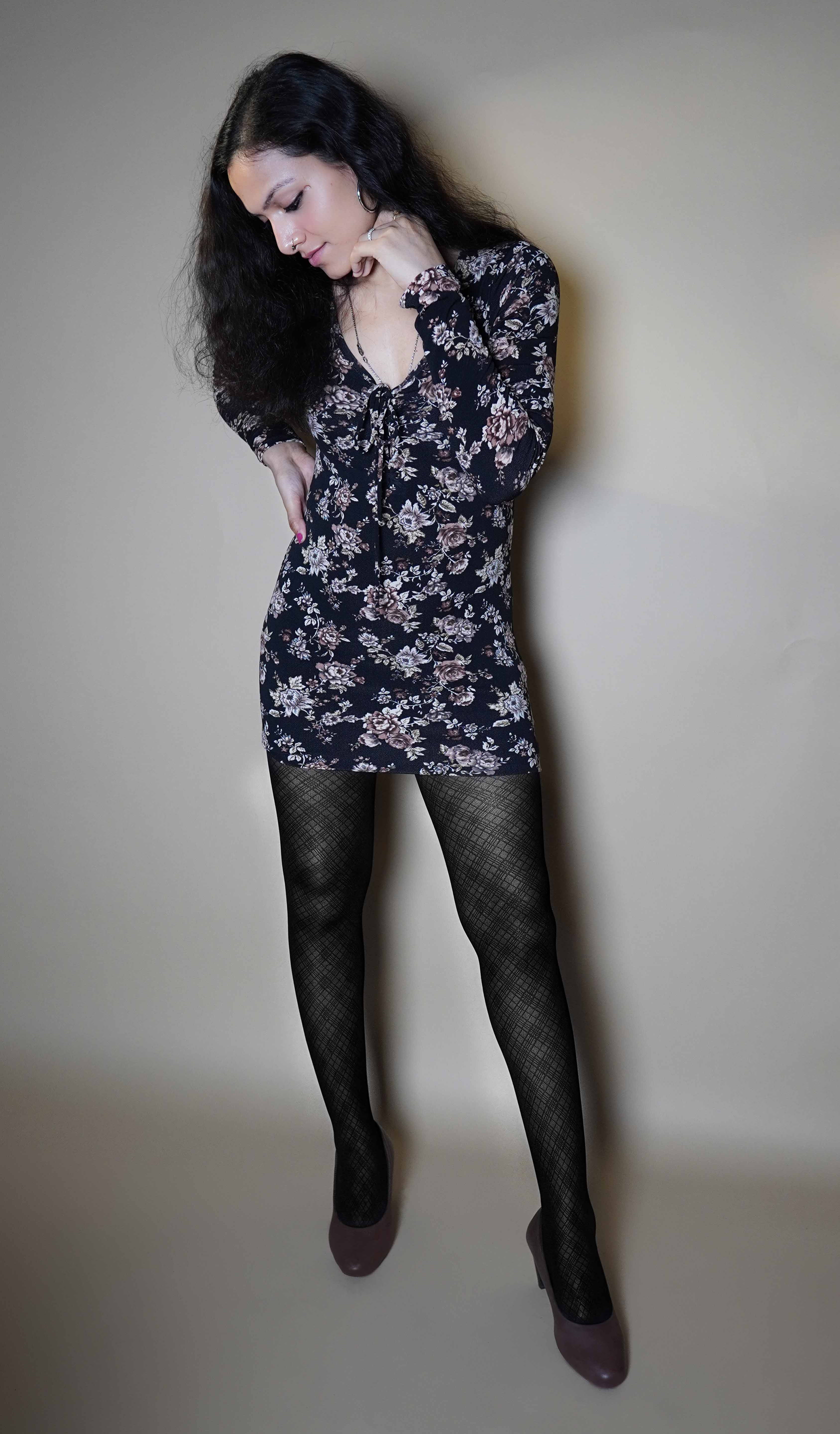 A woman wearing patterned sheer black stocking, posing with her hand on her waist and other gently touching her jawline as she looks downward, highlighting a modish trendy look-Muselot