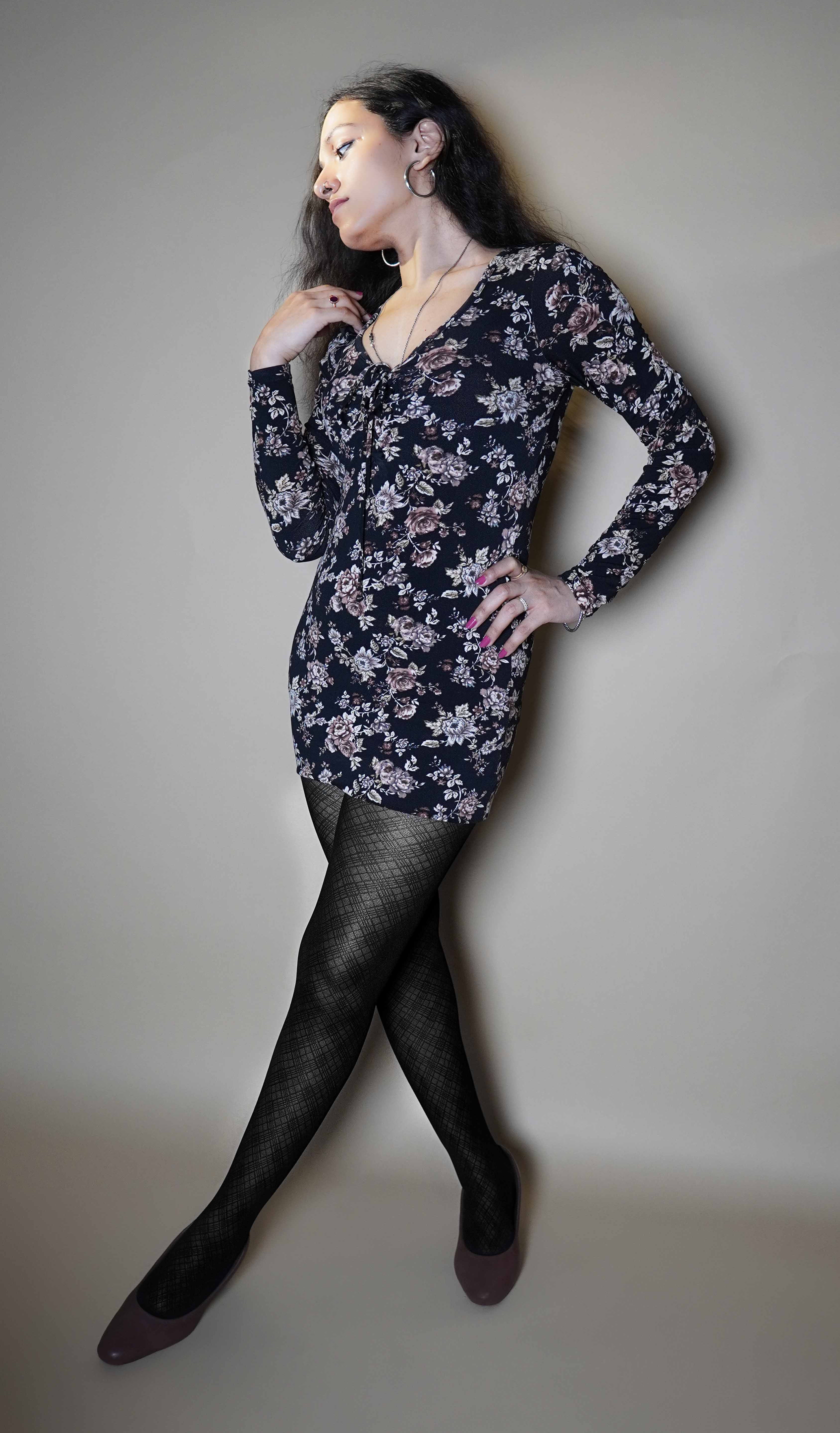 A woman wearing black sheet stockings for girls, posing with her hand on her waist as she looks sideway leaning against a grey wall, showcasing the in demand perfect look-Muselot