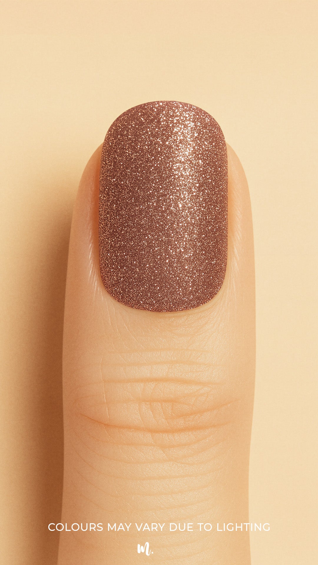 A close-up of a model’s finger wearing Caramel Glow Glitter nail stickies against a beige background, showcasing the warm caramel-brown shade with shimmering glitter, highlighting its radiant glossy finish – Muselot.