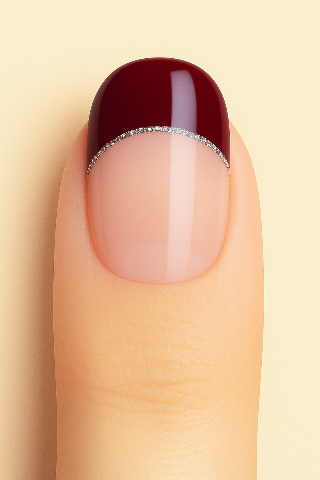 A close-up shot of a model’s finger wearing Cherry Moon French Tip nail stickies, showcasing a deep maroon glossy tip outlined with a fine silver glitter curve over a natural nude base, highlighting a bold and elegant French manicure style with a modern twist – Muselot.