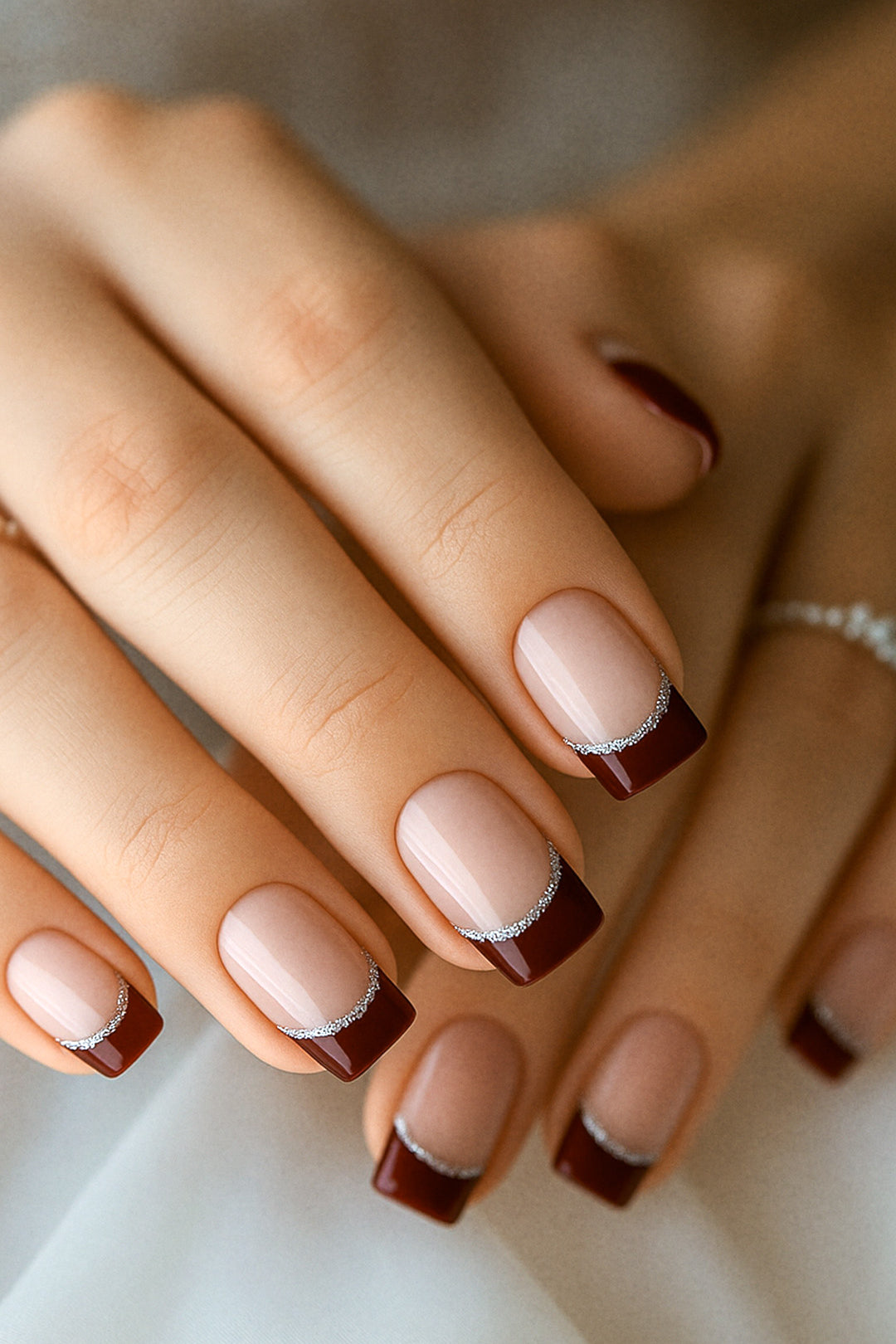 A model’s hand showcasing Cherry Moon French Tip nail stickies, featuring deep maroon glossy tips accented with a fine silver glitter curve over a nude natural base, highlighting the bold yet sophisticated charm of this French manicure design – Muselot.