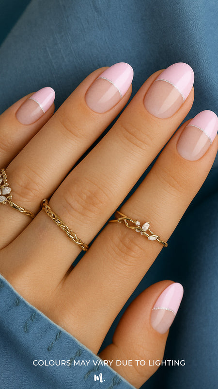 A close-up of a model’s hand featuring the Crowned Petal French Tip nail stickies, designed with a glossy baby pink tip outlined by a fine silver glitter curve over a natural nude base, creating a chic and playful French manicure look – Muselot.