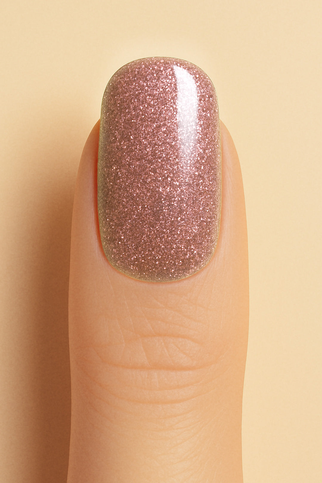 A close-up shot of a model’s finger wearing Dusty Rose Glitter nail stickies, showcasing the soft rose-pink shade filled with fine glitter sparkles, highlighting the elegance and charm of minimal nail art with a shimmering glossy finish – Muselot.