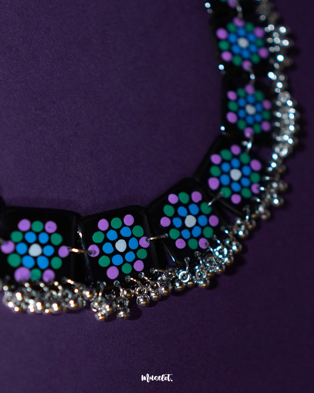 Falak black handmade necklace laid flat, featuring square hand-painted tiles with teal and purple motifs and silver ghungroo trim on a plain backdrop – Muselot.