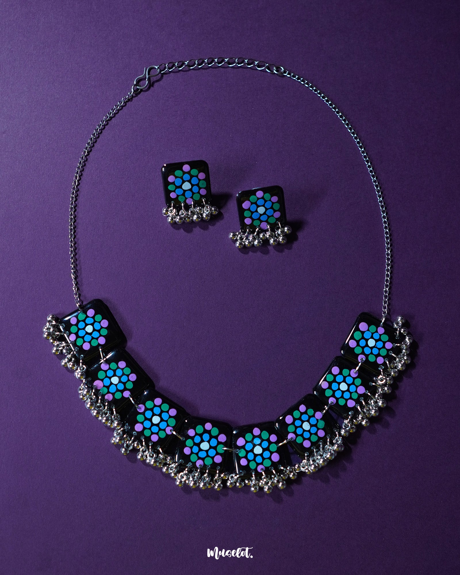 Falak handmade jewelry set featuring black square tiles with teal and purple polka motifs and silver ghungroo accents, including matching earrings, displayed against a purple background – Muselot.