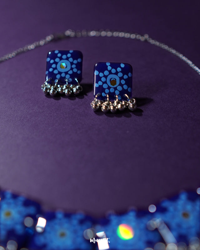 Close-up of the Falakzaar blue earring showcasing intricate floral detailing in white and sky blue against a rich blue base, highlighting the fine hand-painting and craftsmanship — Muselot.