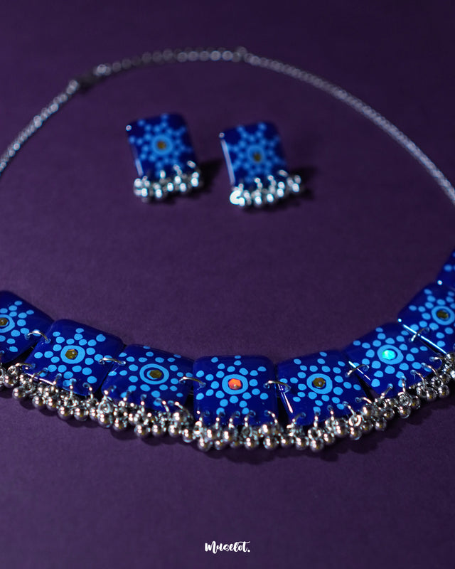 Falakzaar blue necklace and earring set featuring delicate hand-painted floral patterns in white and sky blue on a deep blue base, highlighting the intricate craftsmanship and showcasing graceful ethnic charm — Muselot.