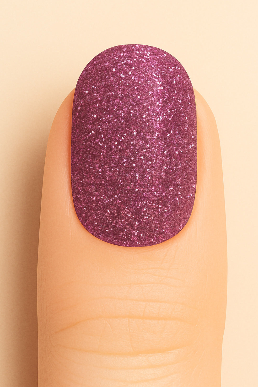 A close-up shot of a finger wearing Glitter Crush nail stickies, showcasing a deep plum-pink shade loaded with fine glitter sparkles, highlighting the rich shimmer and glossy salon-style finish that adds a glamorous pop to the nails – Muselot.