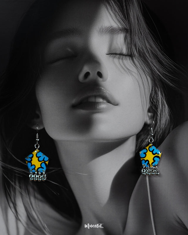 A woman wears the Gulaftab floral hook earrings, showcasing their bold yellow and blue floral patterns with silver bead drops that add a vibrant, handcrafted charm to her look — Muselot.