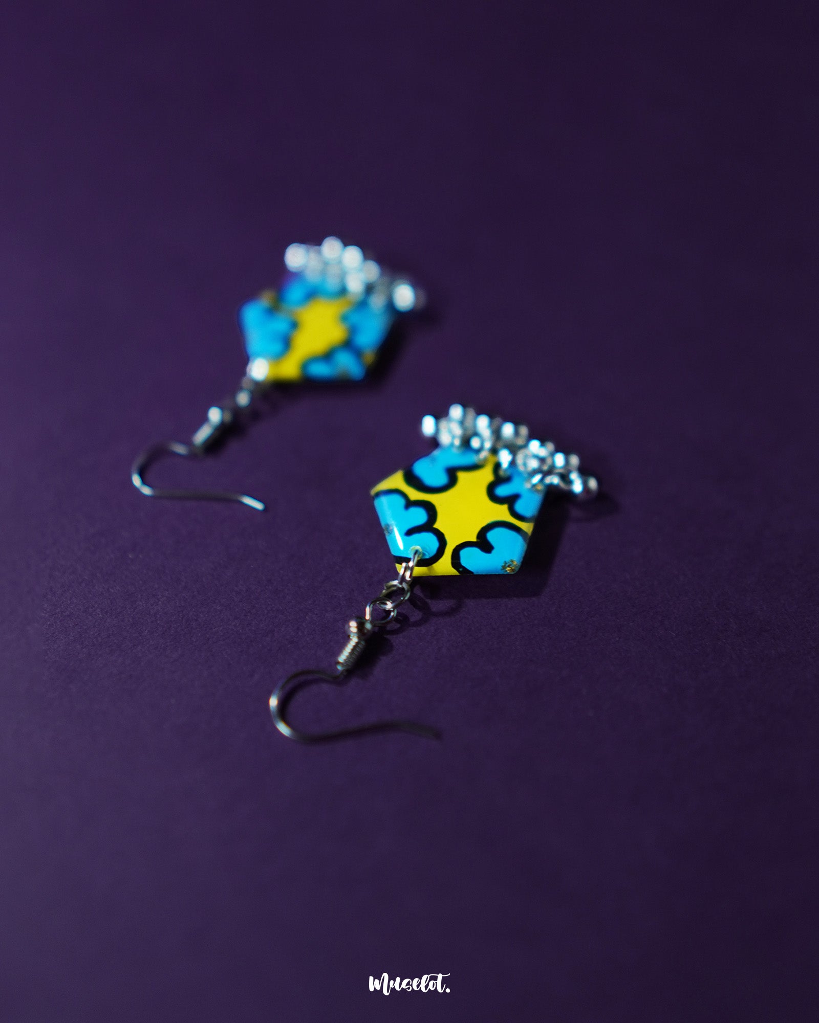 Front view of Gulaftab hook earrings against a purple background, showcasing the vibrant blue floral design on a yellow base with dangling silver beads for a playful yet artistic charm — Muselot.
