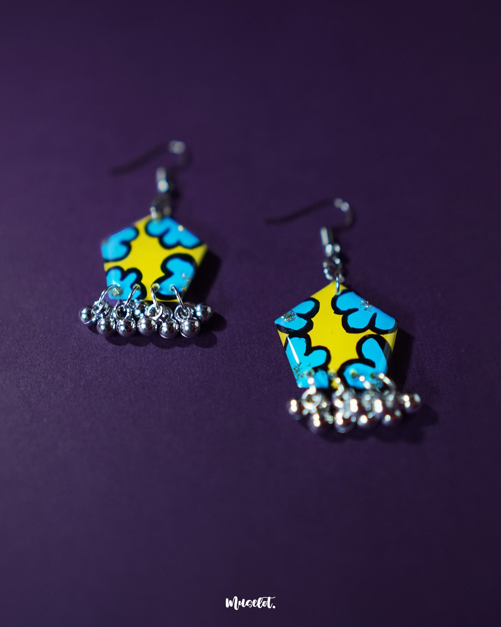 Gulaftab floral hook earrings displayed against a dark background, featuring a striking yellow base with bold blue flower patterns and silver bead hangings that enhance their handcrafted appeal — Muselot.