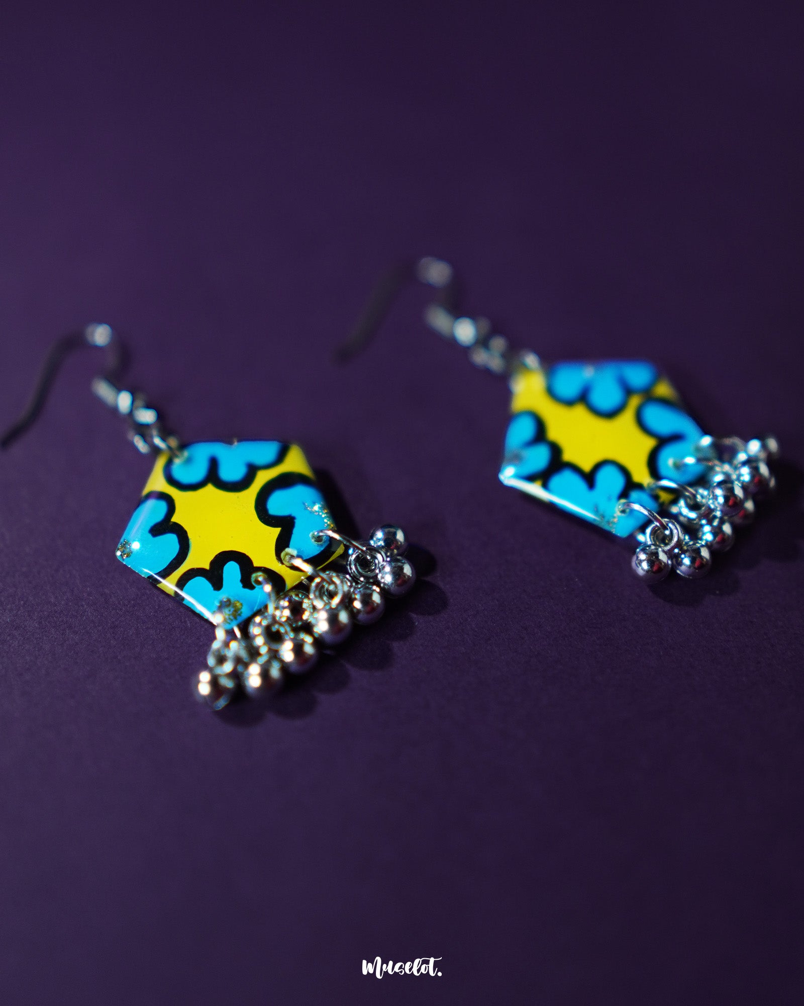 Gulaftab hook earrings shown from a tilted angle, highlighting the hand-painted blue floral design on a mustard-yellow base with delicate silver beads swinging below — Muselot.