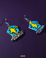Gulaftab hook earrings shown from a tilted angle, highlighting the hand-painted blue floral design on a mustard-yellow base with delicate silver beads swinging below — Muselot.