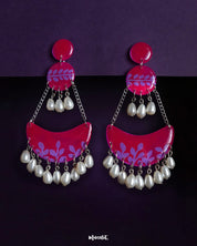 A striking fusion of modern flair and traditional charm, the Gulfaam chandbali earrings feature a hot pink crescent base adorned with purple foliage patterns and cascading pearl drops, creating a look that's both bold and graceful — Muselot.