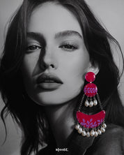 A woman wears the Gulfaam chandbali earrings, where the vibrant hot pink crescent design with lilac botanical motifs and dangling pearl drops adds a bold yet elegant touch to her look, perfectly capturing a playful, festive spirit — Muselot.