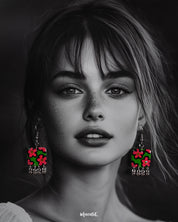 Model wearing the Gulnaar floral earrings, showcasing rectangular charms with bright pink and red flowers on a green background, outlined in black, and accented with delicate silver bead tassels, highlighting their vibrant and playful design – Muselot.
