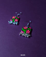 Gulnaar handmade floral hook earrings displayed on a purple background, featuring rectangular charms with vibrant pink and red flowers on a green background outlined in black, accented with delicate silver bead tassels – Muselot.