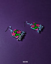 Gulnaar handmade floral hook earrings featuring rectangular charms adorned with bright pink and red flowers on a green background outlined in black, complemented by delicate silver bead tassels, elegantly showcased to highlight their vibrant and artistic design – Muselot.