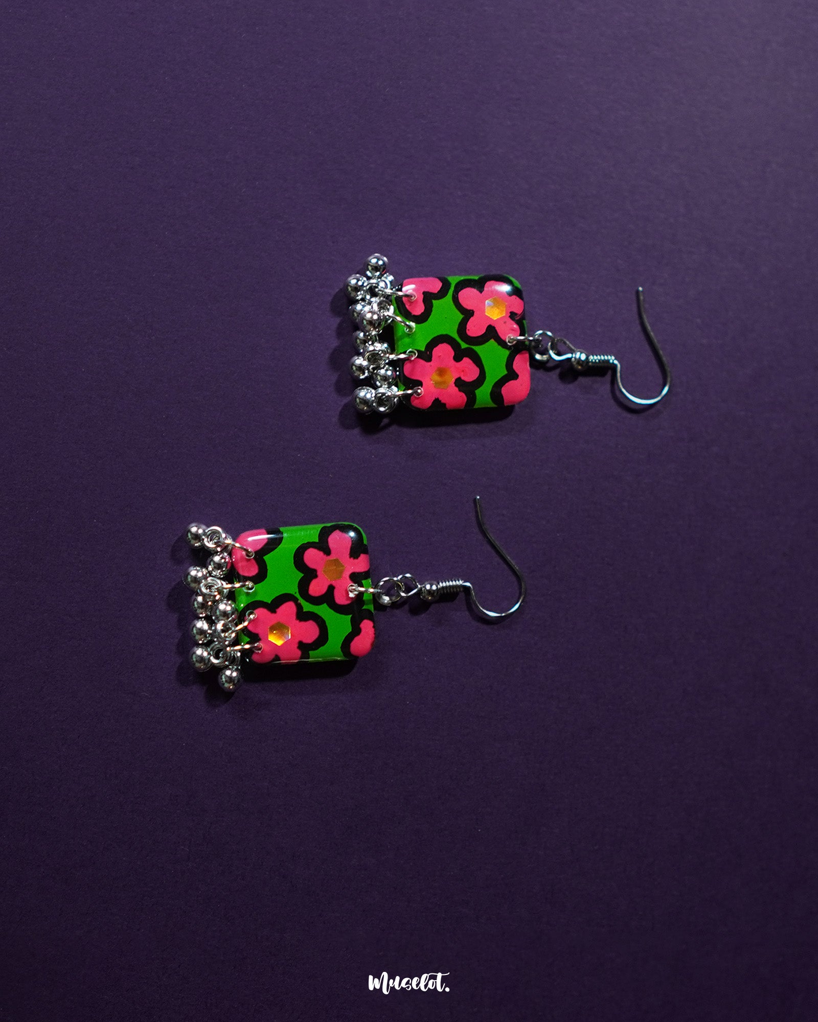 Gulnaar handmade floral hook earrings featuring rectangular charms with bright pink and red floral patterns on a green background outlined in black, adorned with delicate silver bead tassels, artistically displayed to emphasize their vibrant and detailed design – Muselot.