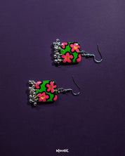 Gulnaar handmade floral hook earrings featuring rectangular charms with bright pink and red floral patterns on a green background outlined in black, adorned with delicate silver bead tassels, artistically displayed to emphasize their vibrant and detailed design – Muselot.