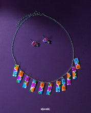 A vibrant close-up of the Gulraas floral necklace set featuring a row of multicolor hand-painted floral charms on a silver-toned chain, paired with matching stud earrings—highlighting its playful charm and boho handcrafted detailing — Muselot