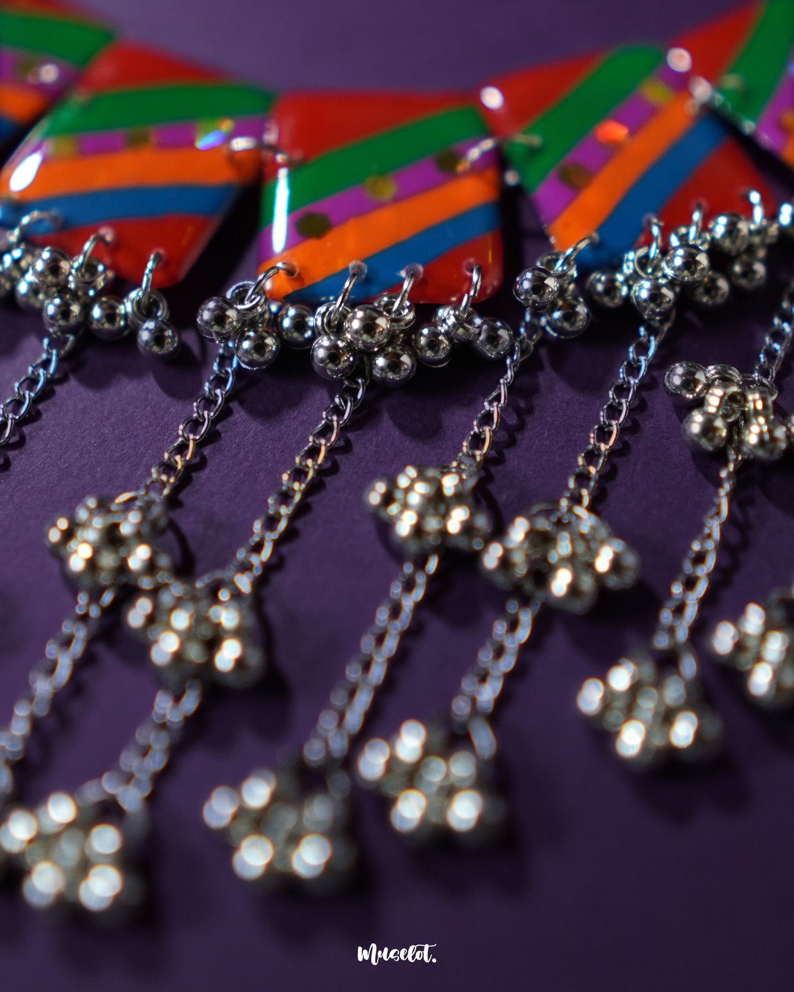 Zoomed-in shot of the Gulrang multicolor resin jewelry set’s ghungroo detailing, showcasing delicate silver bead tassels hanging from bold red, green, blue, and purple striped rectangular charms, highlighting intricate craftsmanship and vibrant design – Muselot.