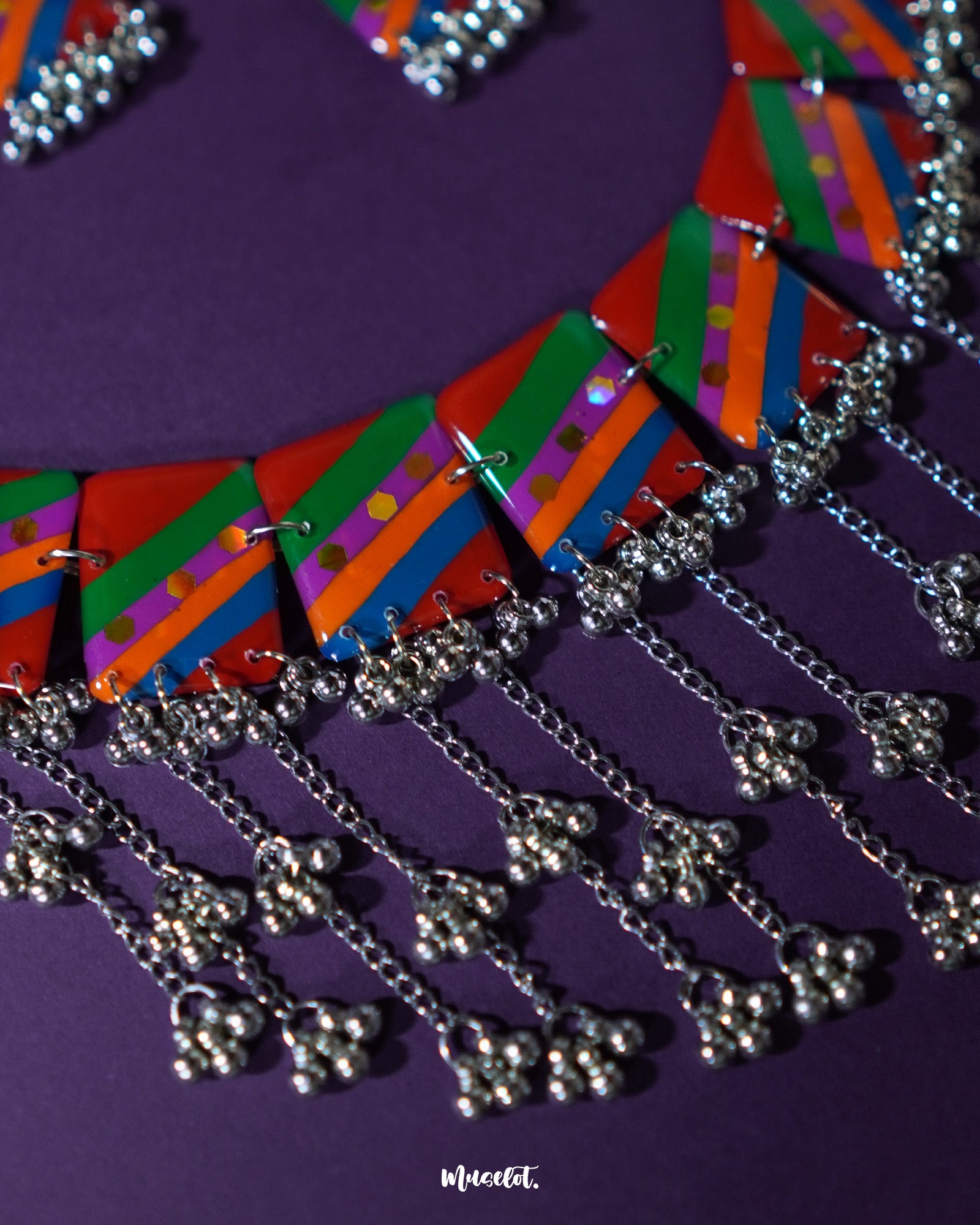 Top-view of the Gulrang multicolor resin jewelry set’s ghungroo detailing, showing delicate silver bead tassels attached to vibrant red, green, blue, and purple striped rectangular charms, highlighting the intricate metalwork and colorful design – Muselot.