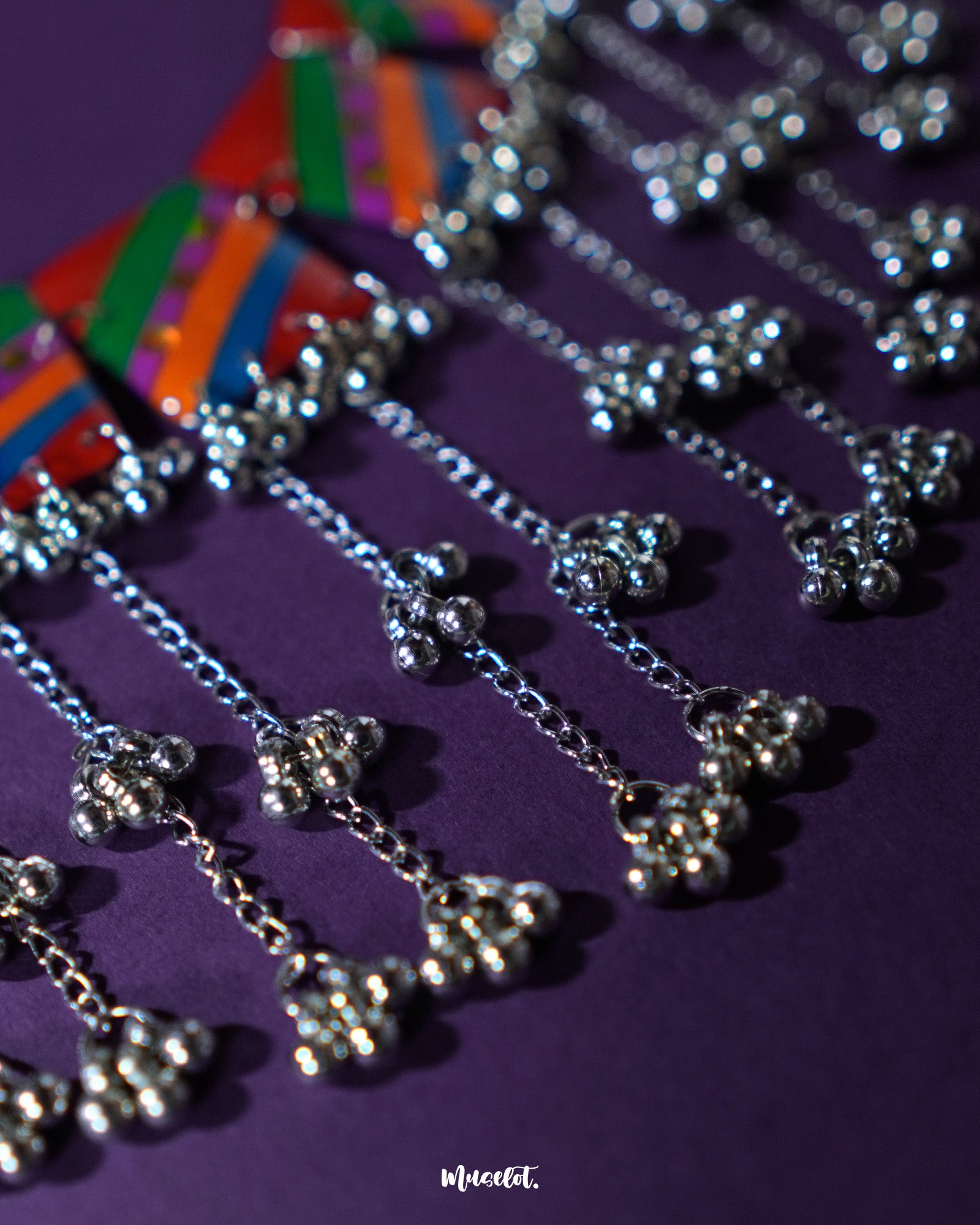 Zoomed-in view of the Gulrang multicolor resin jewelry set’s ghungroo accents, featuring intricate silver bead tassels hanging from bold red, green, blue, and purple striped rectangular charms, showcasing fine craftsmanship and vibrant detailing – Muselot.