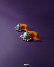 Gulrukh floral jhumkas with yellow and red hand-painted tops and oxidized silver dome drops, showcased against a purple background to highlight their traditional artistry – Muselot.
