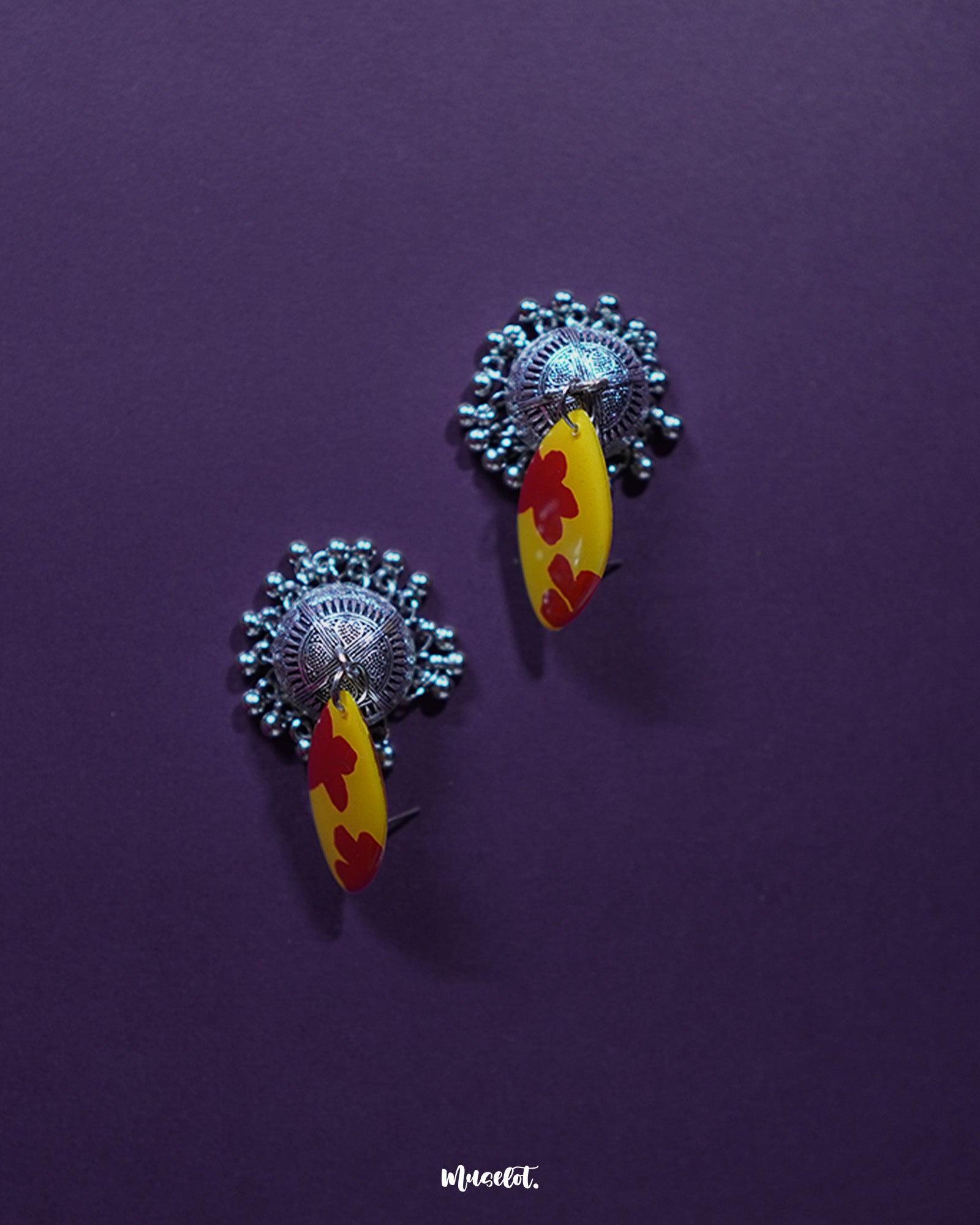 Side angle of Gulrukh floral jhumkas, highlighting the painted floral top and oxidized silver dome with engraved detailing on a plain background – Muselot.