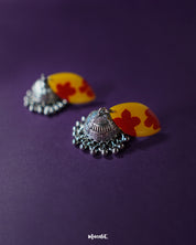 Close-up of Gulrukh floral jhumkas, focusing on the vibrant yellow-red motif and textured oxidized silver dome against a clean backdrop – Muselot.